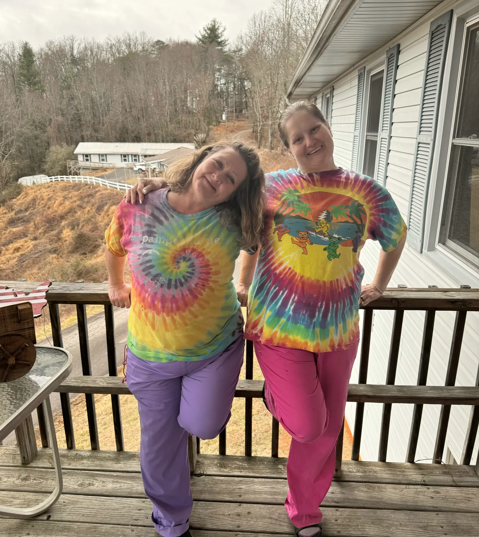 Two women in matching tie-dye shirts, arm in arm on the deck of one of the houses.