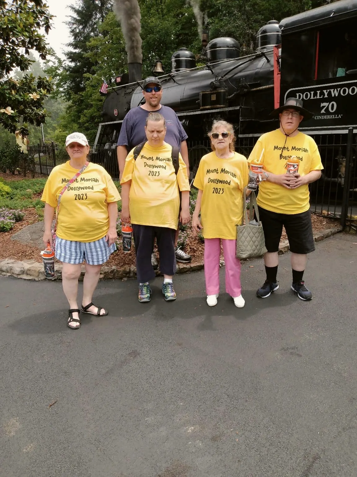 A group in matching yellow T-shirts on a day out, in front of a steam locomotive.