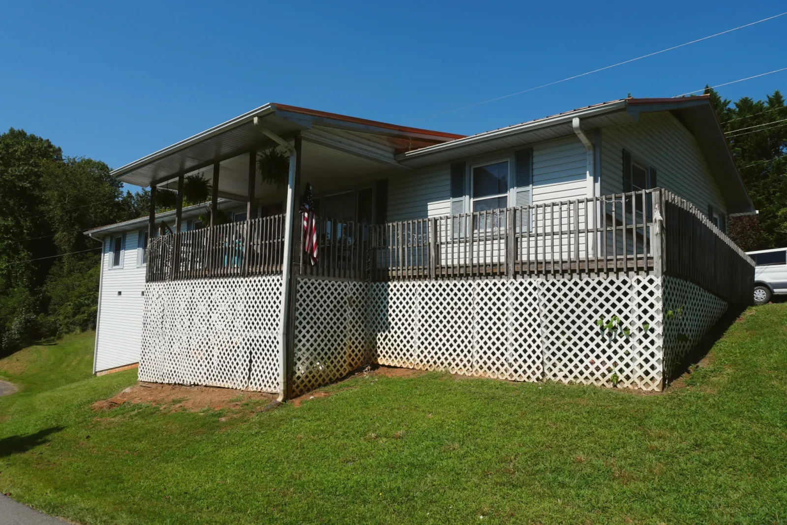 A house with a wide raised deck and white lattice, on a green lawn.