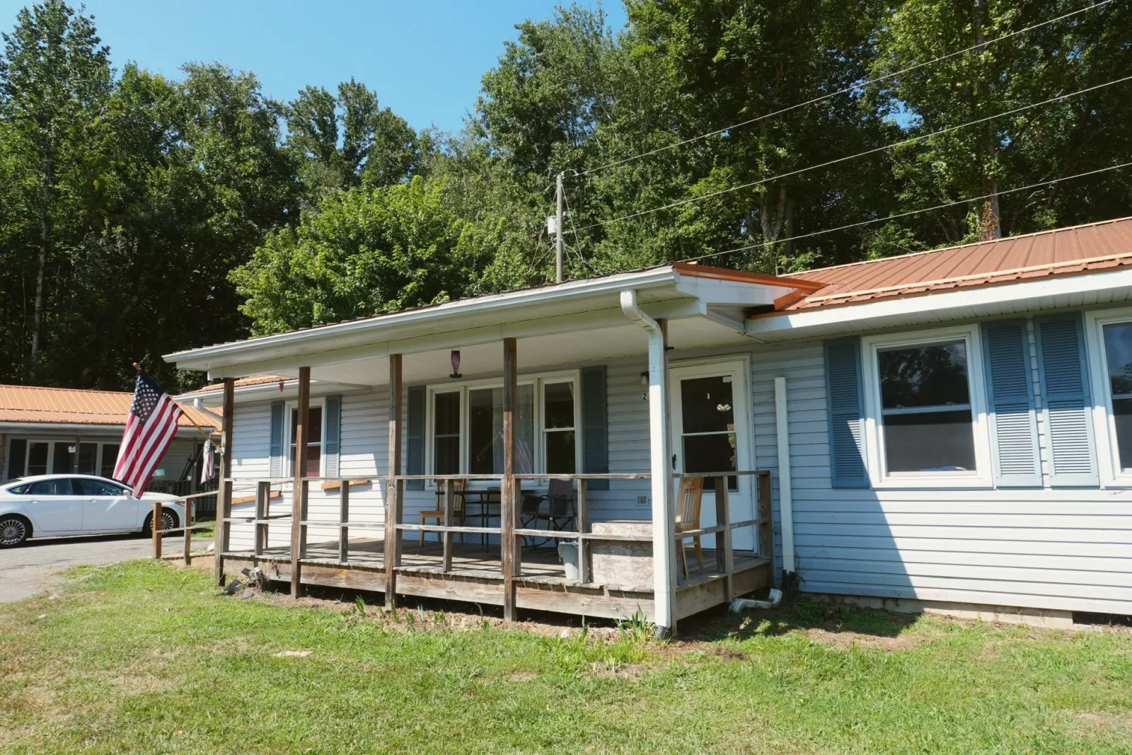 A long single-storey house with a covered front porch, trees behind it.