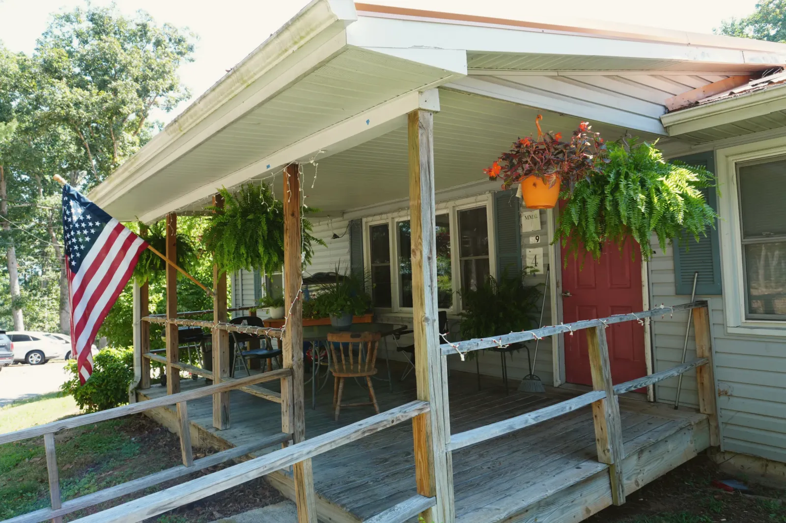 The covered porch of one of the homes: a red front door, hanging baskets and a flag.