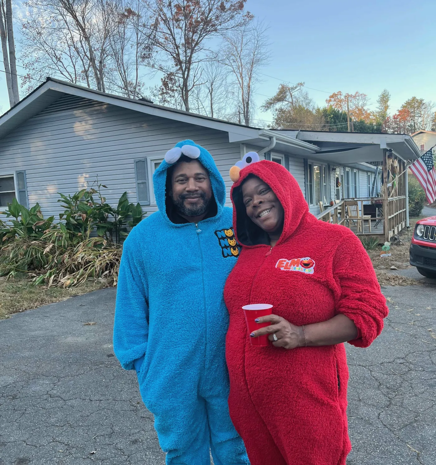 Two people in bright onesies, smiling, outside one of the houses.