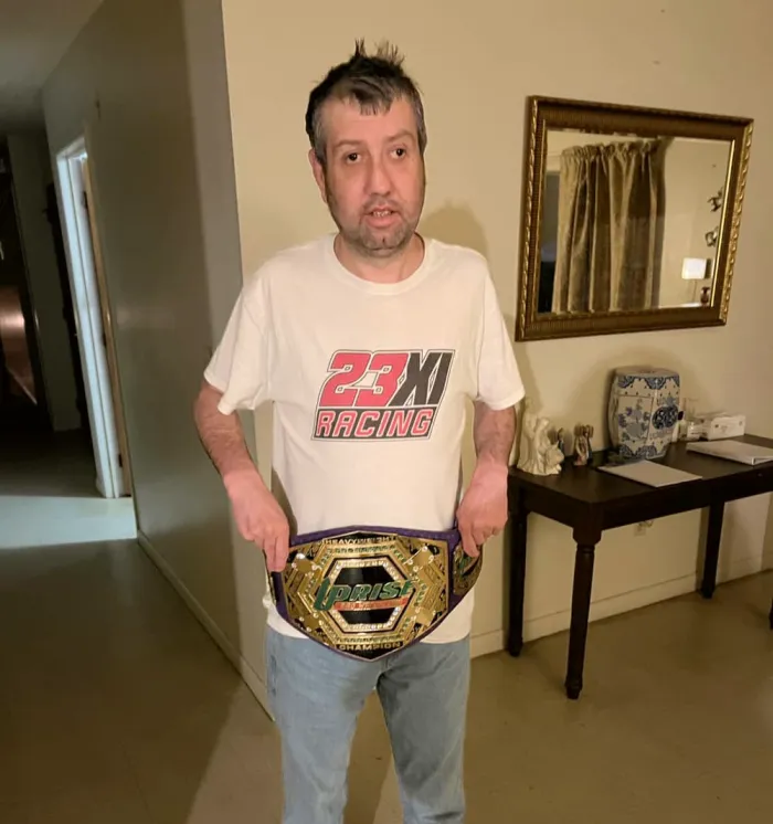 A man proudly holding a championship belt in a hallway.
