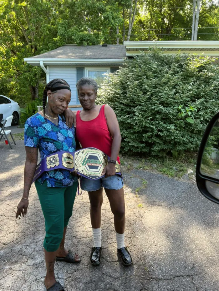 Two women outside, one holding up a championship belt.