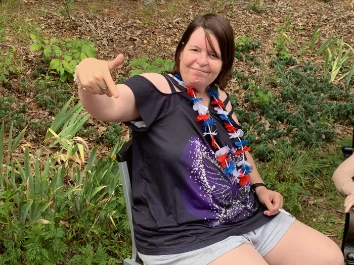 A woman in a festive lei pointing at the camera, smiling.