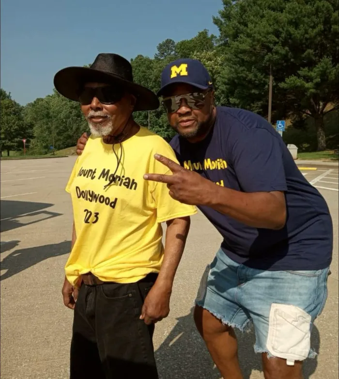 Two men in event T-shirts, one making a peace sign.