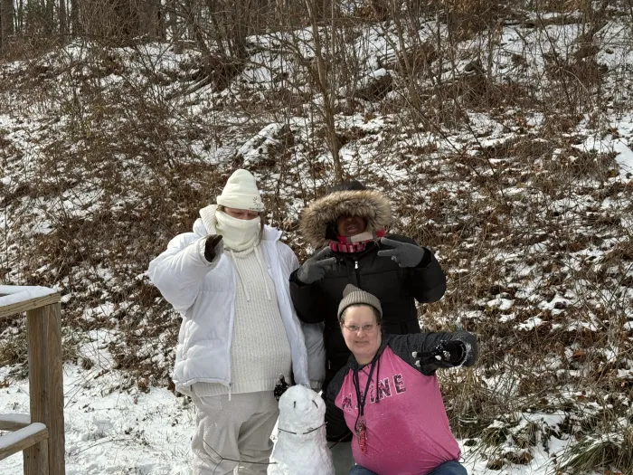 Three people bundled up in the snow outside one of the houses.