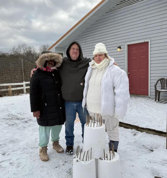Three people in winter coats beside a snowman.