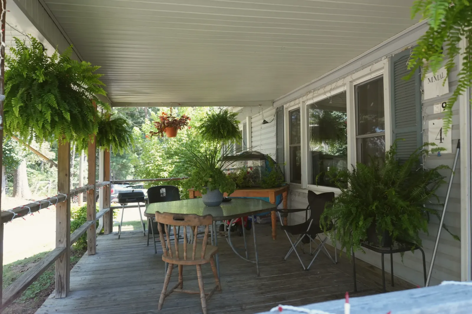 A covered porch set with a table and chairs, ferns hanging from the eaves.