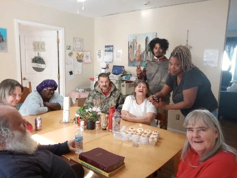 Residents and staff around a kitchen table, laughing.
